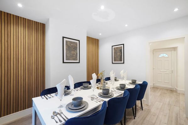 A dining area with a long table set for six, blue chairs, and framed artwork on the walls. - Charming 3-bedroom house in welcoming London neighborhood (london)