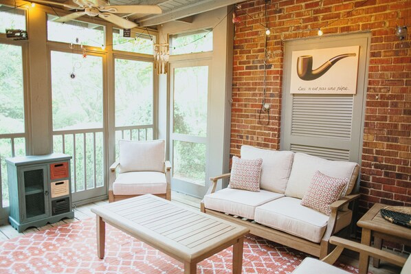A cozy room with a brick wall, a white sofa with patterned cushions, a wooden table, and a small cabinet.