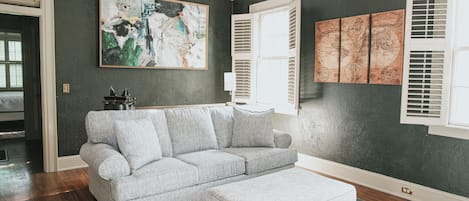 Una sala de estar con un sofá modular, un otoman a juego, un cuadro abstracto grande y un mapa mundial en la pared.