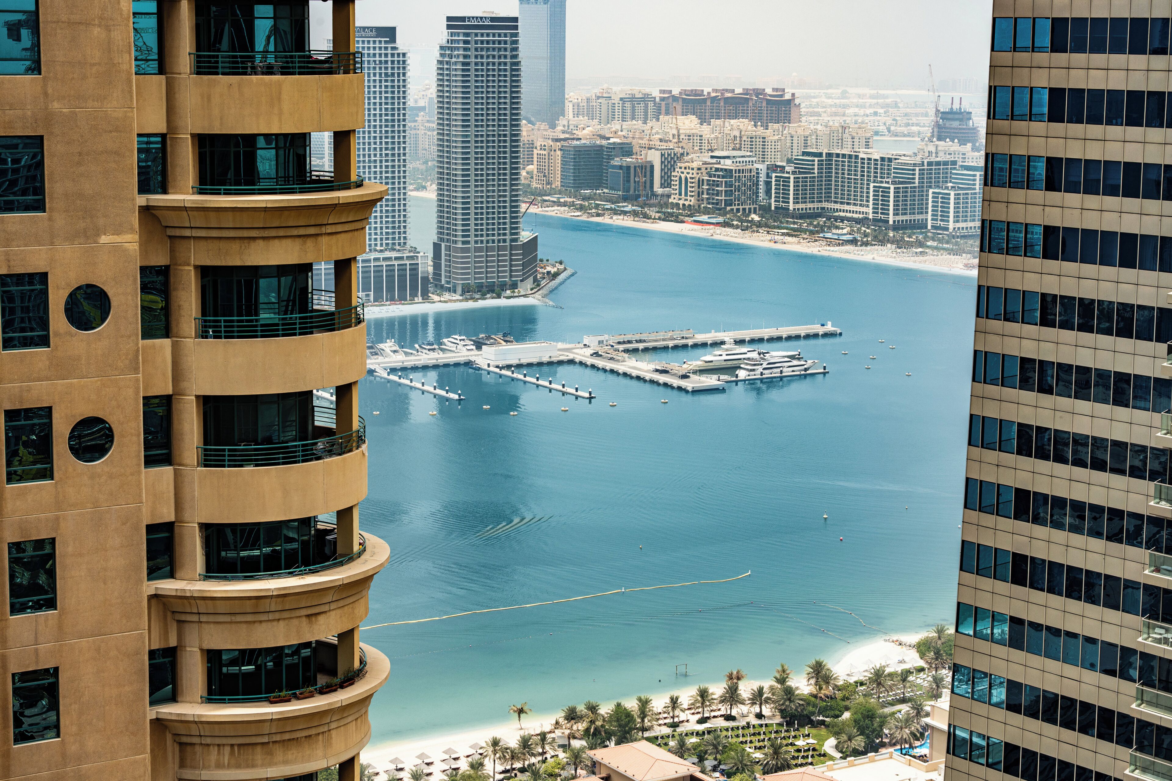 A high-rise building with a marina and a beach in the background.