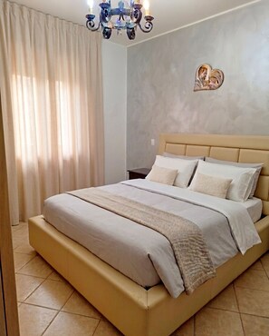 A bedroom with a bed, curtains, a chandelier, and a wall decoration. - An apartment in the heart of the village where you can enjoy your family vacation. (Montenero di Bisaccia)