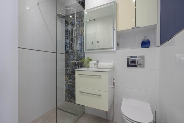 A modern bathroom with a glass shower enclosure, a white toilet, and a vanity with a mirror. - Cosy Studio with a Balcony | Close to the Park (Warszawa)