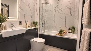 Un baño moderno con salpicadero de mármol, una bañera independiente, un inodoro y un lavabo con mueble.
