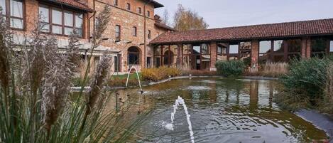 A courtyard with a pond, a brick building, and a covered structure.
