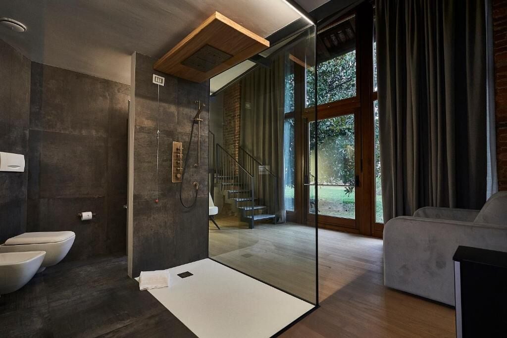 A modern bathroom with a glass shower enclosure, a visible staircase, and a view of the outdoors.