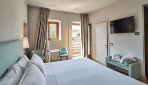 A hotel room with a large bed, a desk, a chair, a TV, and a balcony.