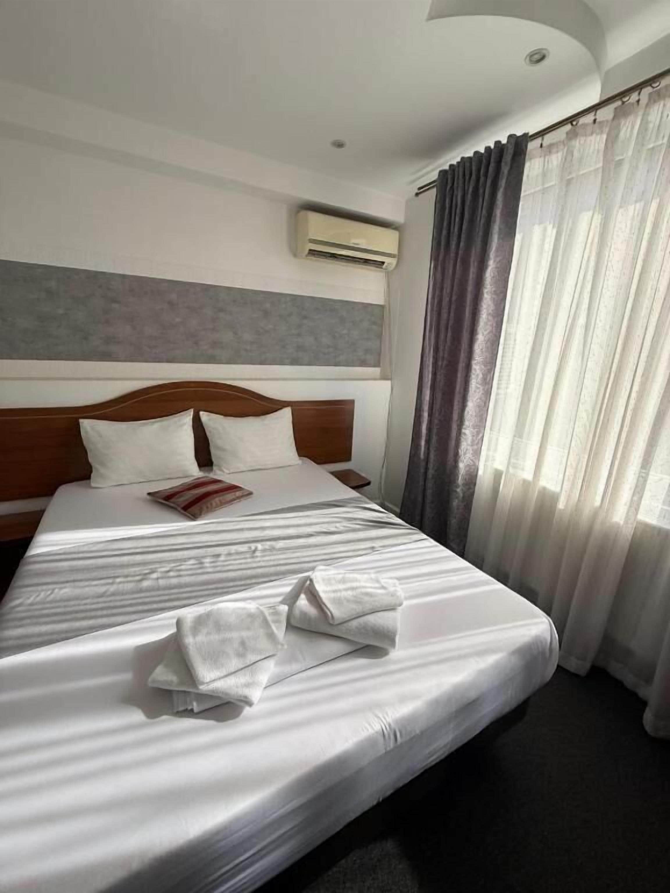 Une chambre d’hôtel avec un grand lit, une tête de lit, un appareil de climatisation et une fenêtre avec des rideaux.