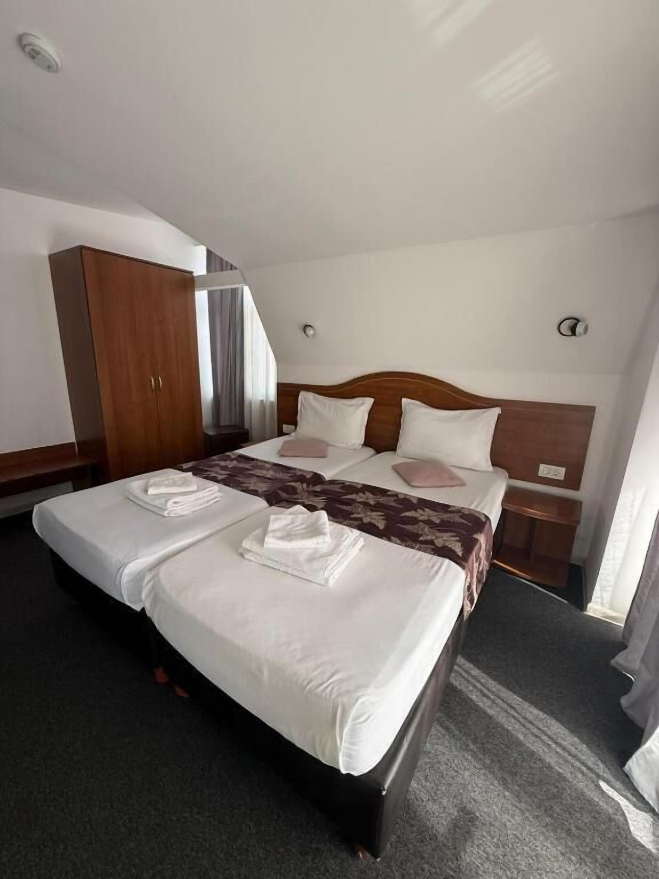 A hotel room with a large bed, a wardrobe, a bedside table, and a window with curtains.