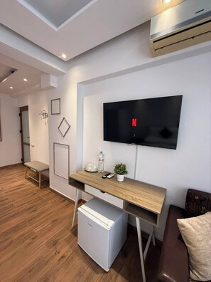 Una sala de estar moderna con un televisor de pantalla plana montado en la pared, un escritorio de madera, un mini refrigerador blanco, un banco y un sofá de cuero marrón.