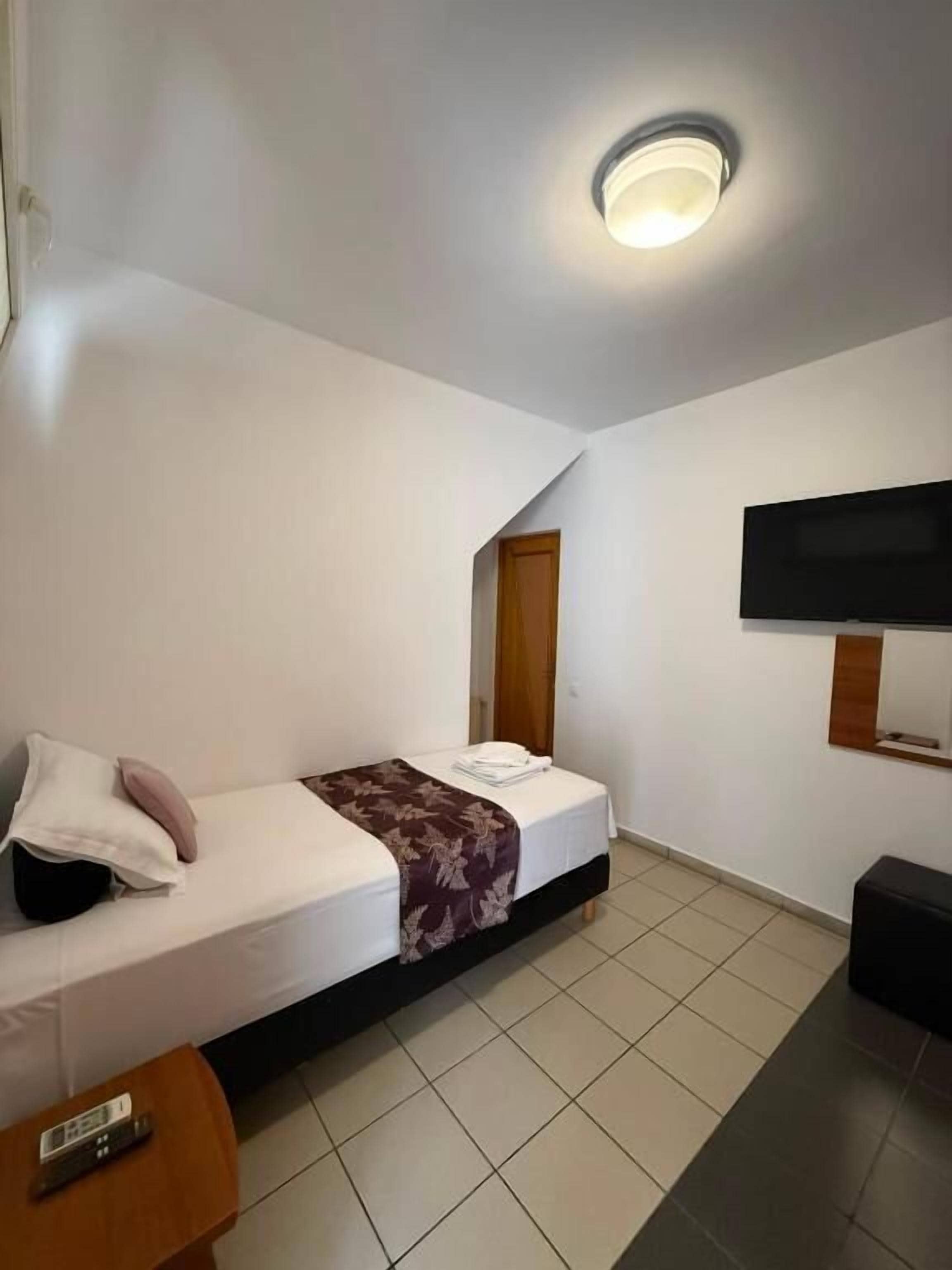 Habitación de hotel con cama, televisor montado en la pared, una mesita y un control remoto sobre ella.