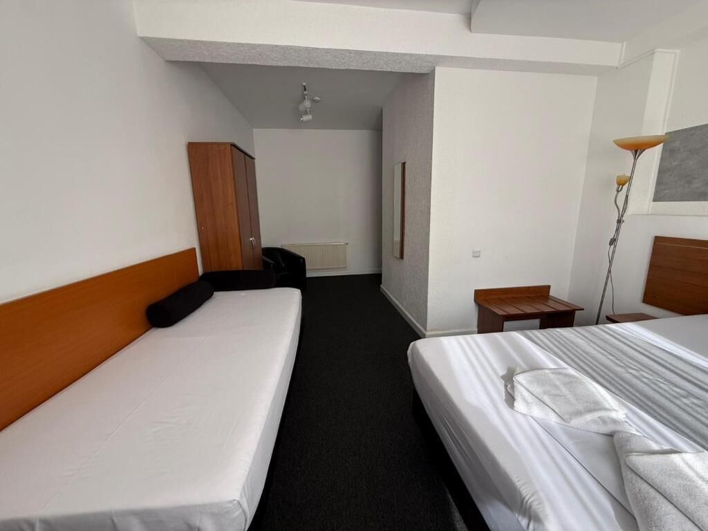 Une chambre d’hôtel avec deux lits, une tête de lit en bois, une petite table, une lampe et un radiateur.