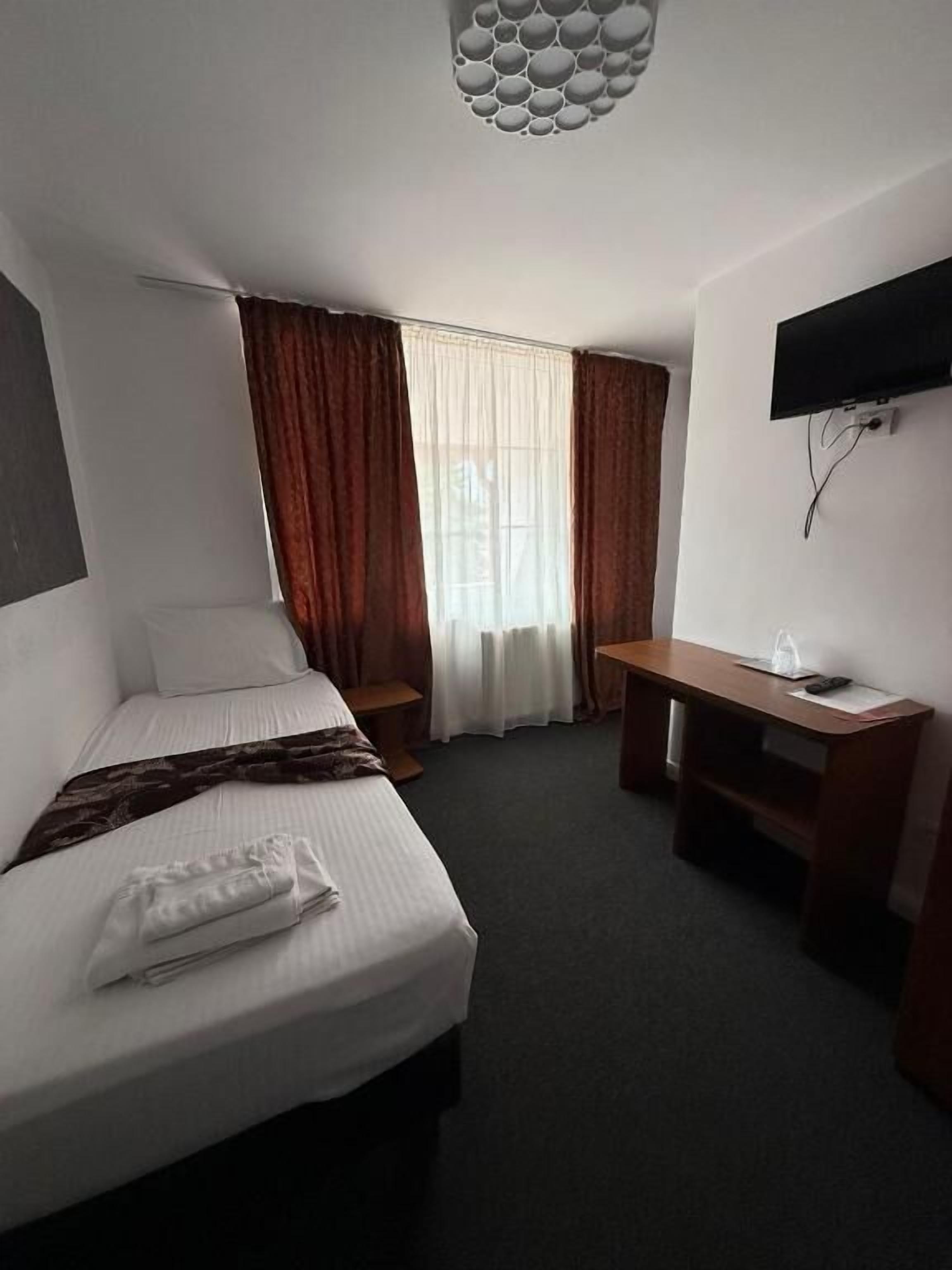 A hotel room with a bed, a desk, a chair, a television, and a window with curtains.