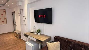 A modern living room with a flat-screen TV mounted on the wall, a sofa, a small table, and an air conditioning unit.