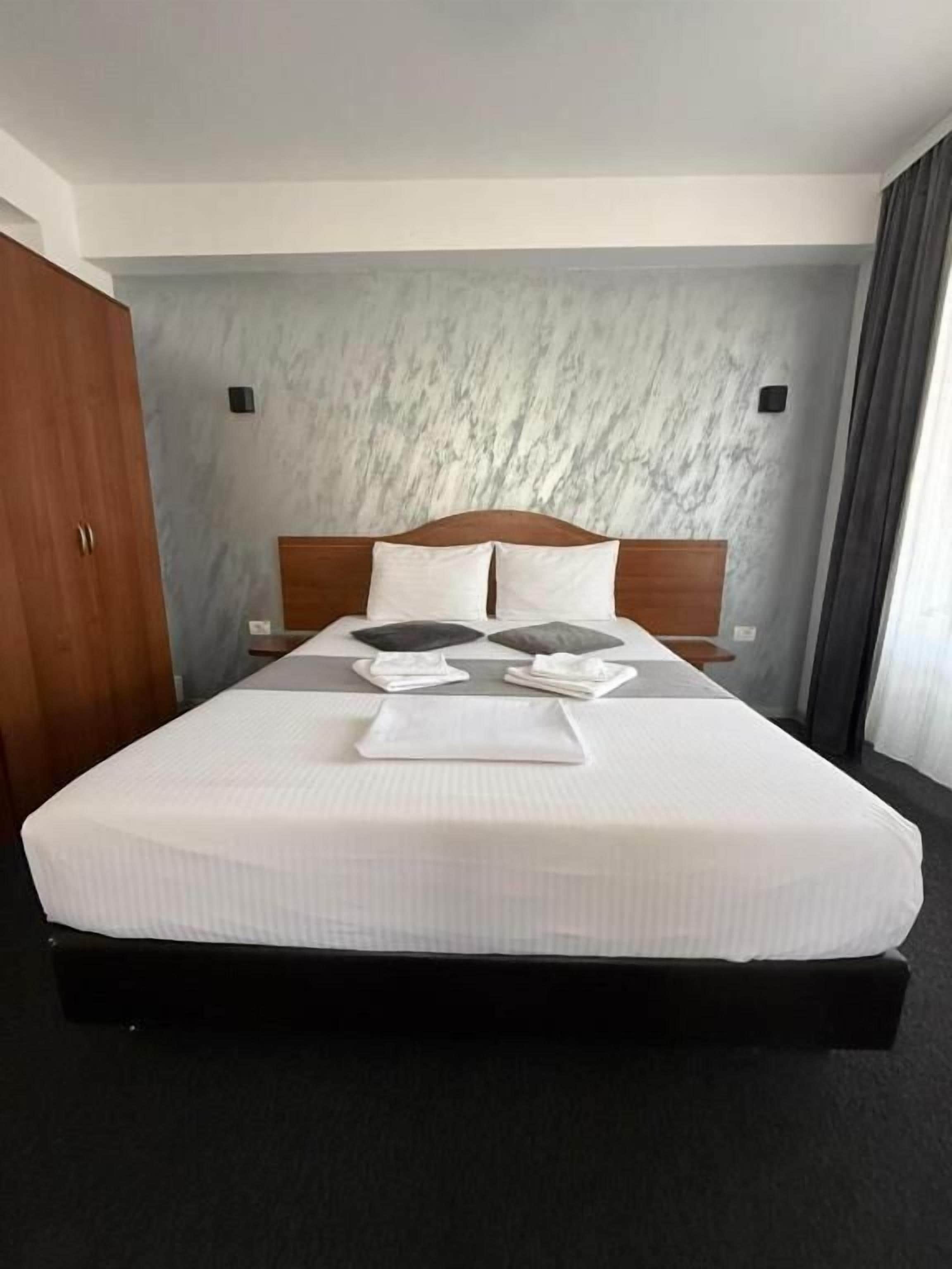 Une chambre d’hôtel avec un grand lit, une tête de lit en bois, un mur en marbre et une moquette sombre.
