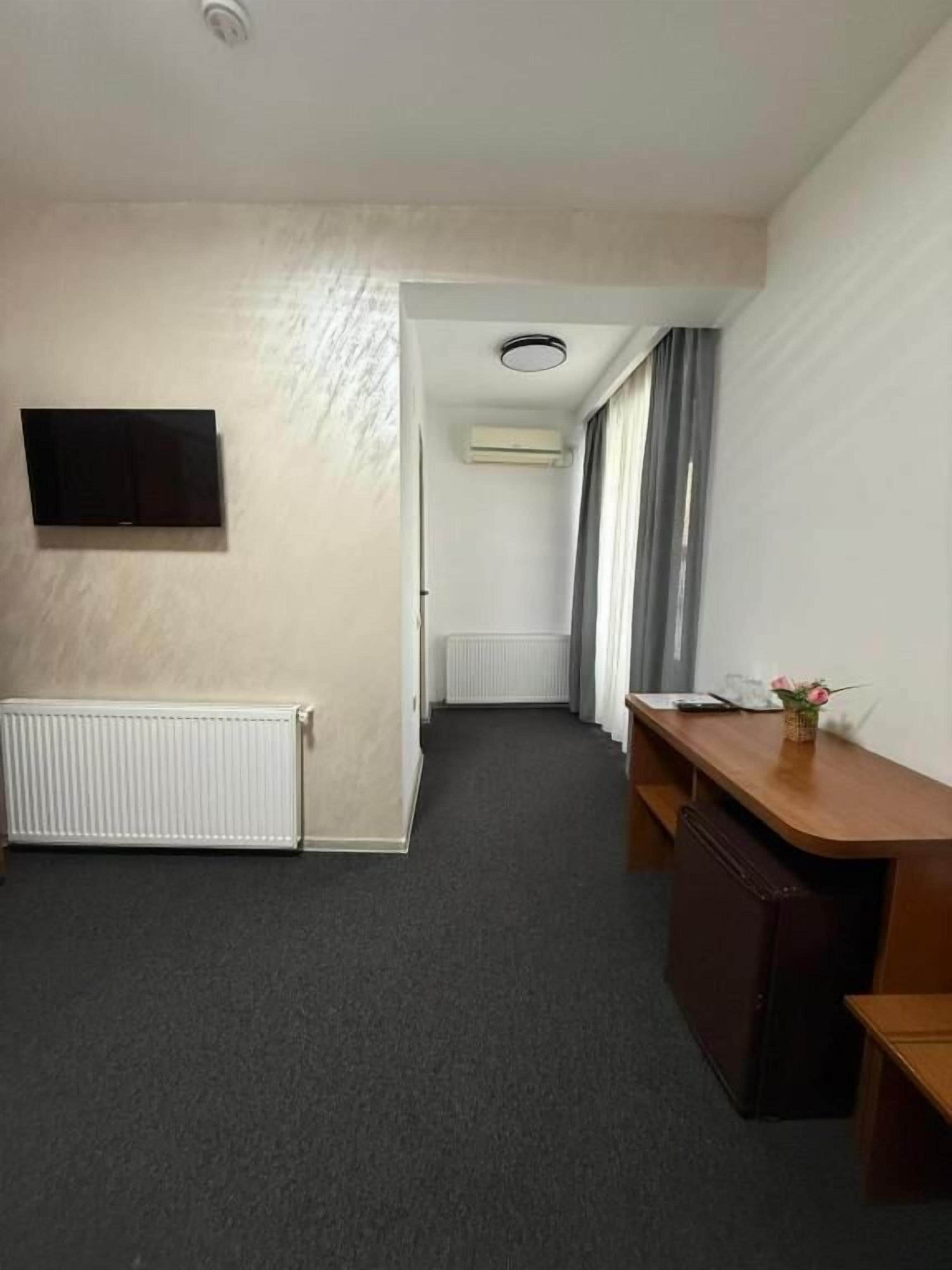 A hotel room with a bed, a desk, a chair, a television, and a window with curtains.