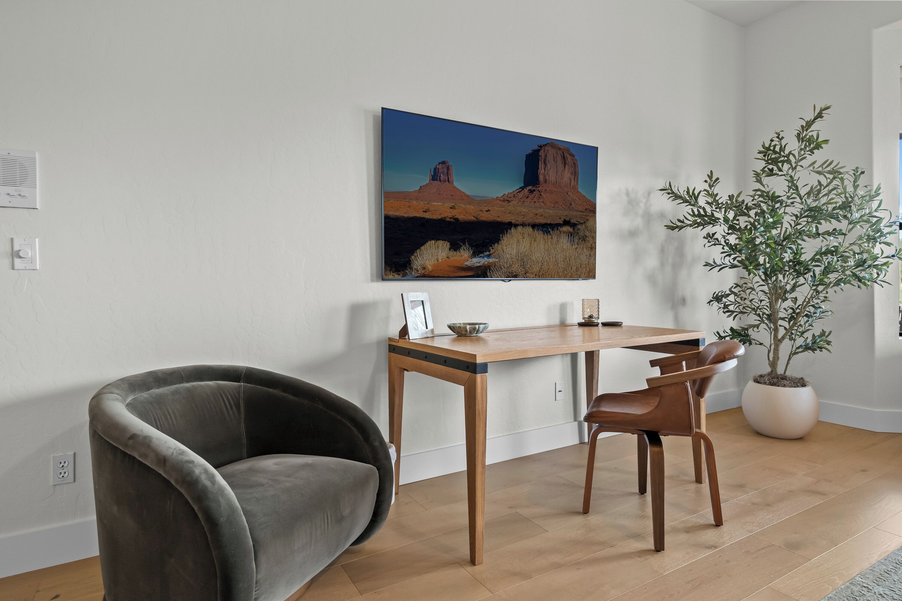 A room with a desk, two chairs, a potted plant, and a painting on the wall.