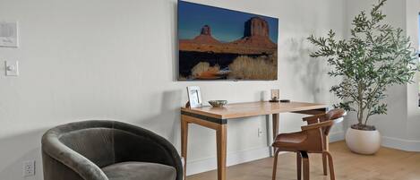 A room with a desk, two chairs, a potted plant, and a painting on the wall.