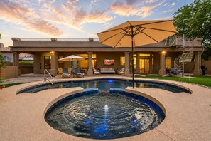 A swimming pool with a sunken center, surrounded by lounge chairs and umbrellas, with a building in the background. - Casa Mesa - Luxury Golf Retreat, Pool & Spa, All King Beds (Mesa)