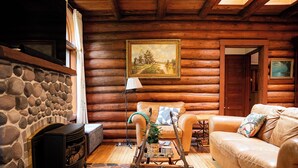 A log cabin interior with a stone fireplace, a sofa, a rocking chair, and a painting on the wall. - Storybook stone & log cabin with barrel sauna, 2 min to the beach (Herbster)