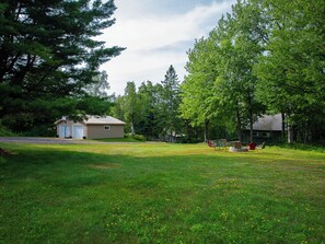 A grassy area with a small cabin and a larger building surrounded by trees.