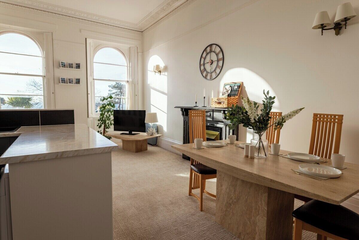 A modern kitchen with a dining area, large windows, and a clock on the wall.