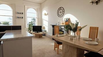 A modern kitchen with a dining area, large windows, and a clock on the wall.