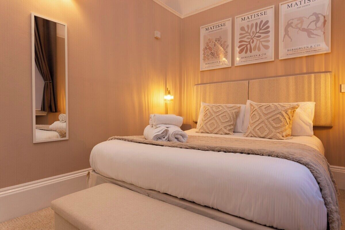 A hotel room with a large bed, a bedside table, a mirror, and wall art.