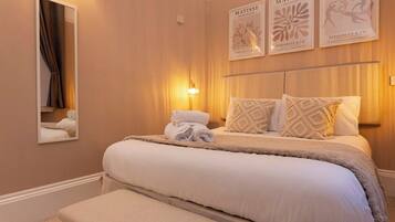 A hotel room with a large bed, a bedside table, a mirror, and wall art.