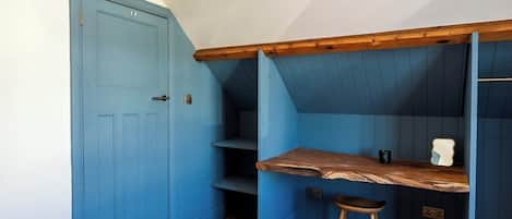 A room with a blue door, a wooden desk, a stool, and a slanted ceiling.