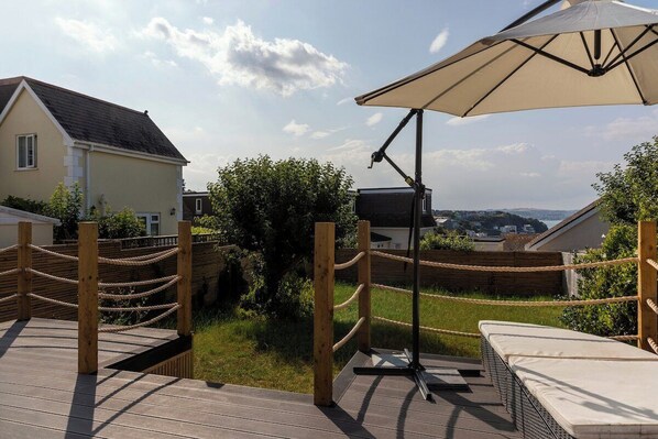Eine Terrasse mit Geländer, Liegestuhl und Sonnenschirm.