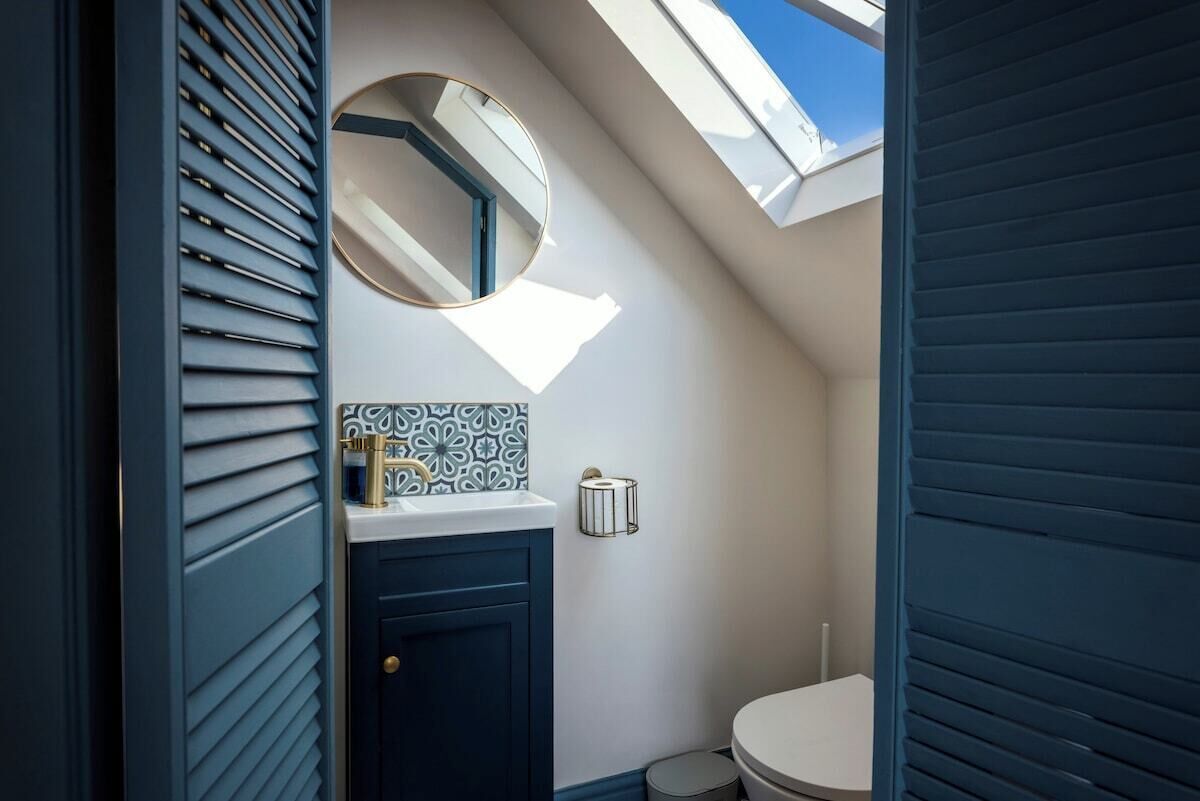 Un bagno con una finestra a lucernario, uno specchio rotondo, un water e un pannello decorativo.