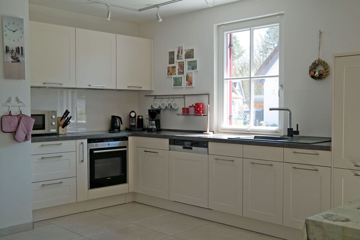 A modern kitchen with white cabinets, a dishwasher, an oven, and a window providing natural light.