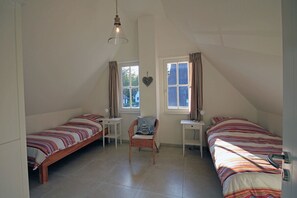 Une chambre avec deux lits simples, une chaise, un bureau et une fenêtre.