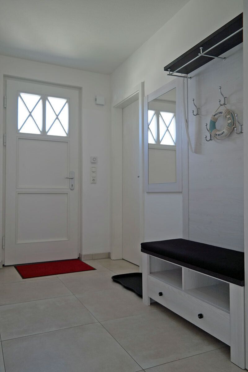 A hallway with a white door, a bench, a red mat, and a coat rack with hangers.