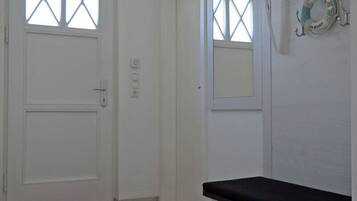 A hallway with a white door, a bench, a red mat, and a coat rack with hangers.