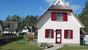 A white house with red shutters, a thatched roof, and a small garden.