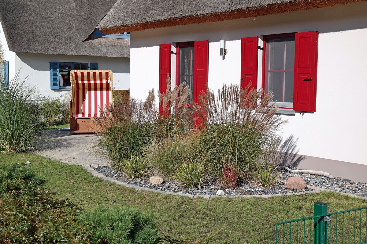 A white building with red shutters and a thatched roof.
