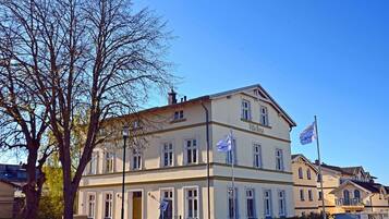 Ein zweigeschossiges Gebäude mit der Aufschrift 'Villa Rosa' an der Fassade, zahlreichen Fenstern und Flaggen auf Fahnenmasten.