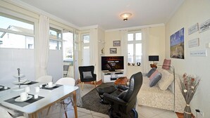 A modern living room with a television, seating area, and dining space. - Just 35 meters from the sandy Baltic Sea beach, Wi-Fi, 2 bedrooms, sleeps up to 5 people, with a balcony (Glowe)