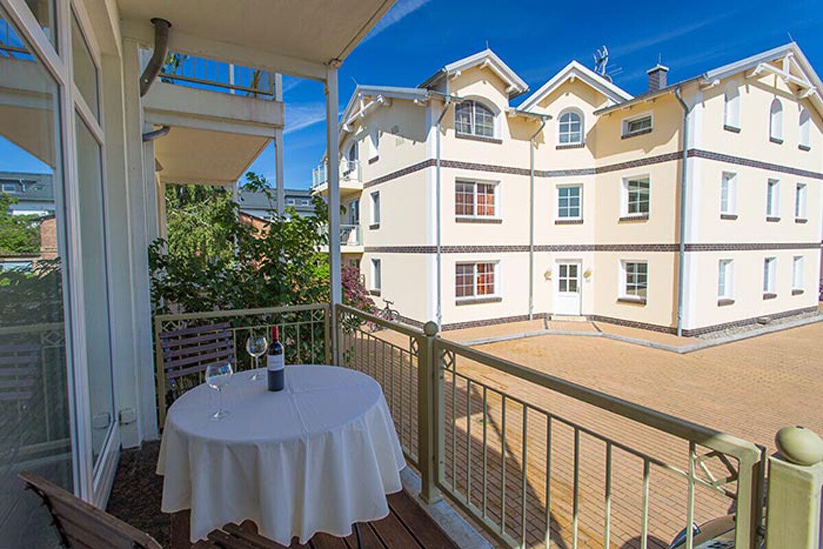 A balcony with a table set for two, overlooking a building with multiple windows and balconies.