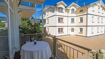 A balcony with a table set for two, overlooking a building with multiple windows and balconies.