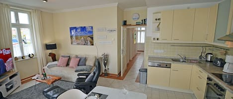 A living room with a sofa, a dining table set for two, and a kitchen with cabinets and appliances.