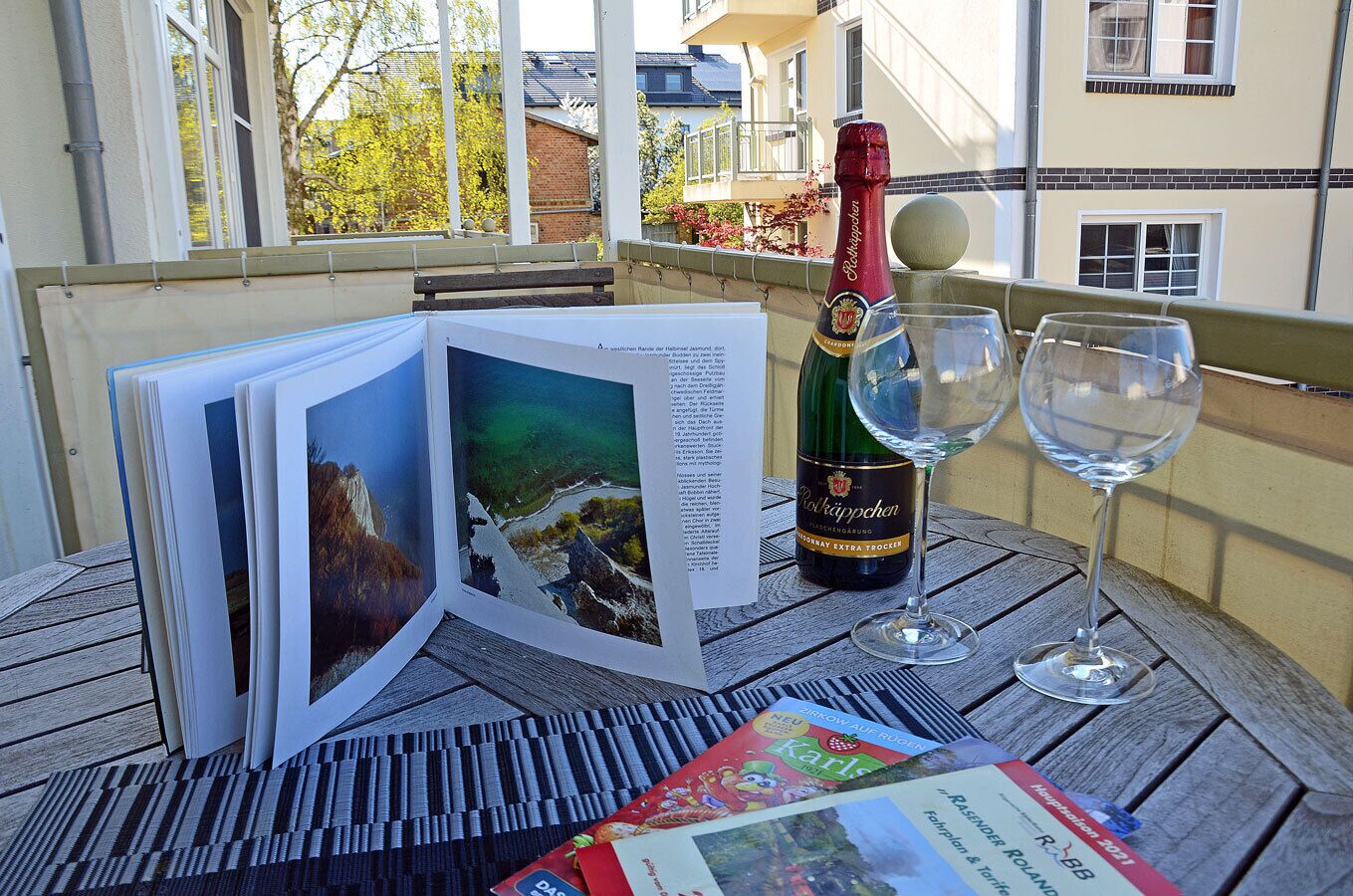 Une table avec une bouteille de vin, deux verres et un livre illustré de paysages.