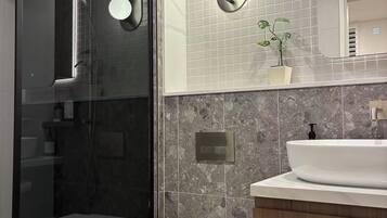 A modern bathroom with a glass shower enclosure, a white toilet, a vanity with a sink, and a mirror with integrated lighting.