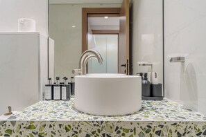 Une salle de bain avec un lavabo blanc, un robinet moderne et un comptoir recouvert de carreaux.