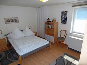 Ein Schlafzimmer mit einem Bett, einem Sessel, einem Bücherregal und einem Fenster.