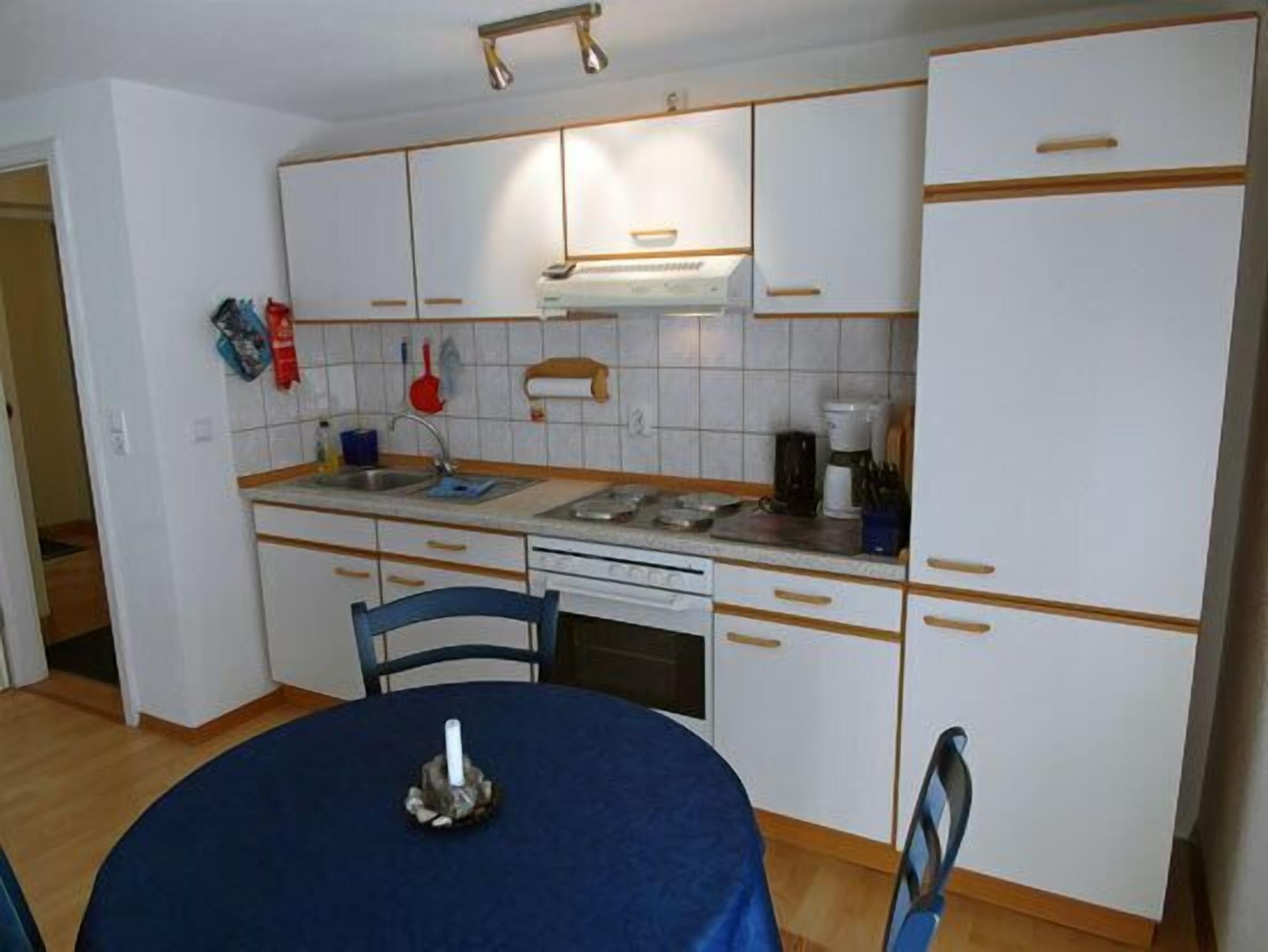Una cocina compacta con armarios blancos, una mesa de comedor con mantel azul y una cafetera.