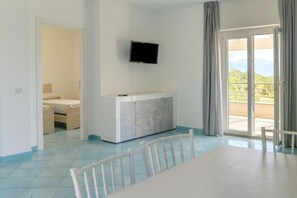 Une pièce comprenant une table à manger, un téléviseur fixé au mur, un balcon avec vue et un lit dans la pièce adjacente.