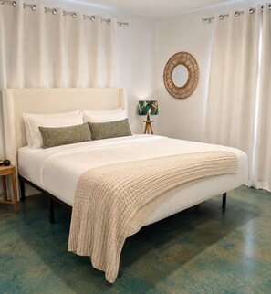 A bedroom with a bed, a bedside lamp, a wall-mounted mirror, and curtains. - Punta Gorda Paradise – Spacious 4-Bedroom Getaway (Punta Gorda)