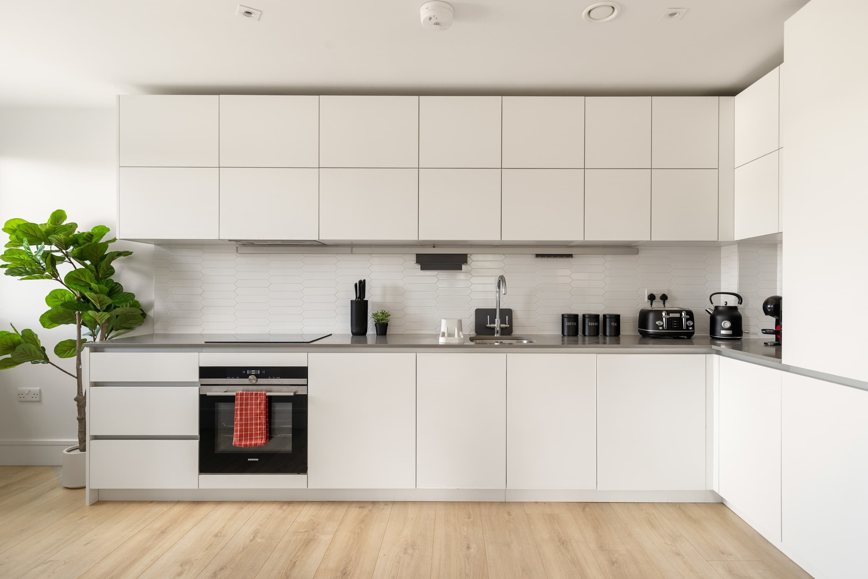 A modern kitchen with white cabinetry, a built-in oven, a coffee machine, and a plant.